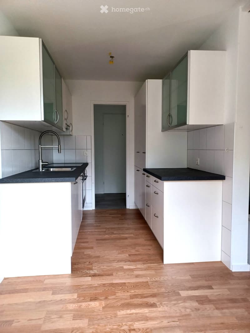 Modern kitchen with white cabinets, black countertops, and a wooden floor. Features a sink with a modern faucet and a doorway leading to another room.