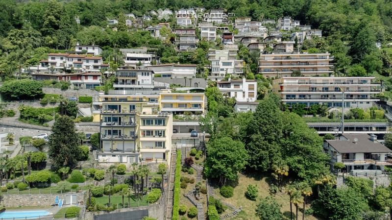 Aerial view of a hillside residential area with multiple houses, balconies, and a swimming pool in the foreground.