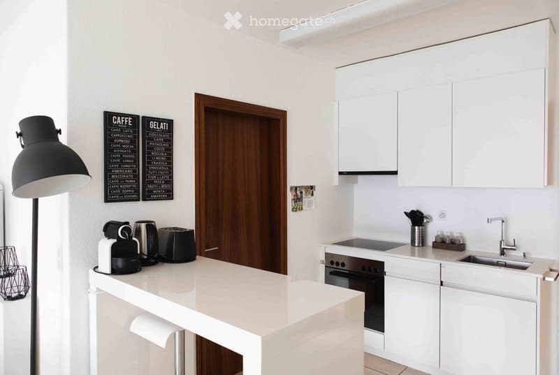 Modern kitchen with white cabinets, stainless steel appliances, and a white countertop. Features a coffee maker, toaster, oven, and sink with a modern faucet.