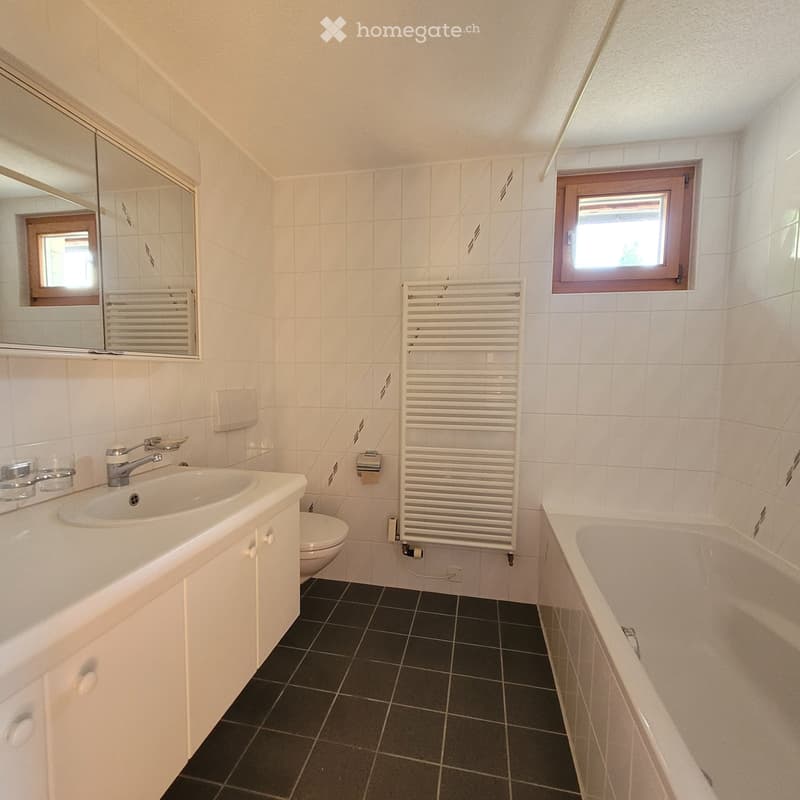Modern bathroom with white tiles, black floor tiles, a sink with a faucet, a mirror, a toilet, a bathtub, and a radiator.