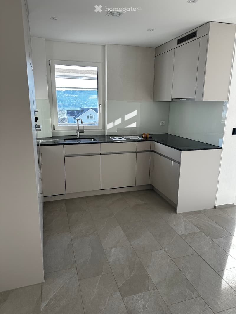 Modern kitchen with grey cabinets, black countertop, and a large window offering a scenic view.