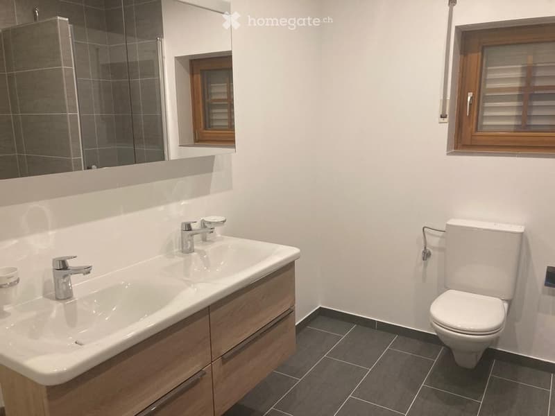 Bathroom. Modern bathroom with double sink, wooden cabinet, chrome faucets, toilet, and large mirror. Dark tiled floor and white walls.