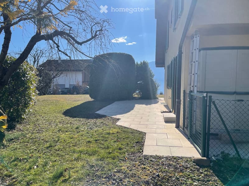 Garden / Outdoor Area. A well-maintained garden area with a paved pathway leading to a house entrance, surrounded by greenery and a fence.