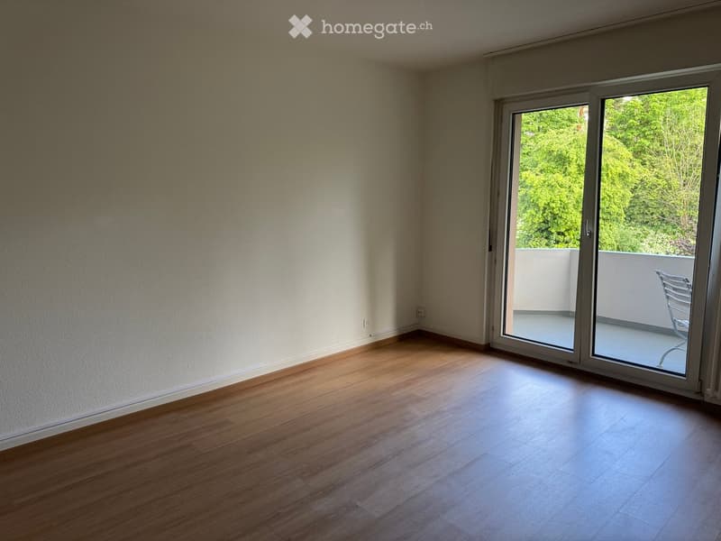 Empty room with wooden flooring, large sliding glass door leading to a balcony with outdoor chair visible.