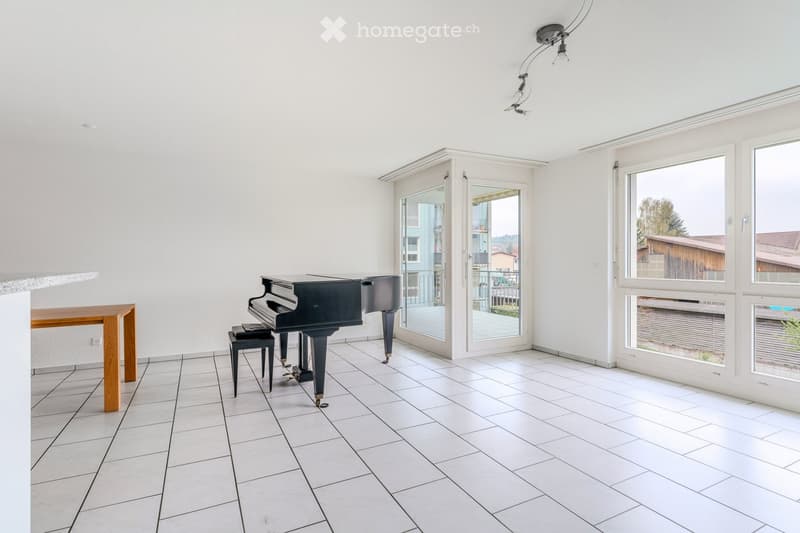 Bright, unfurnished room with white tiled flooring, large windows, and a grand piano with a matching bench. A small wooden table is positioned against the wall.