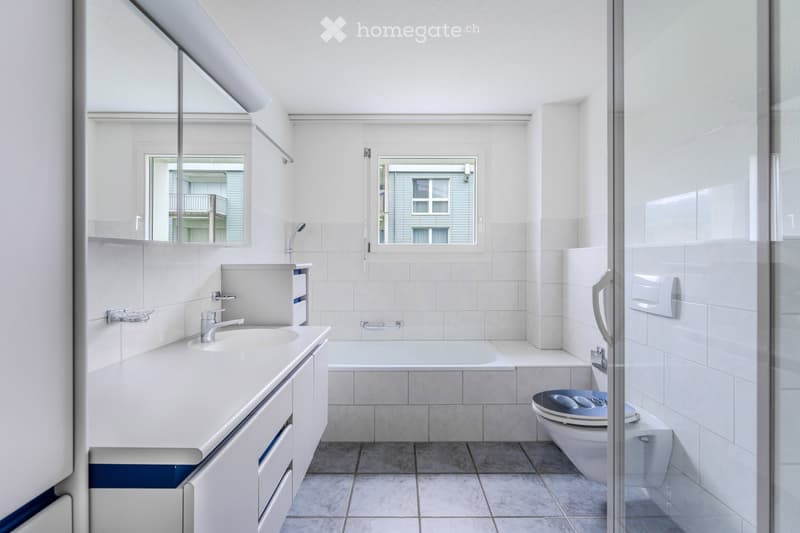Modern bathroom with white tiles, a sink with a faucet, a bathtub, a toilet, and a large mirror above the sink.