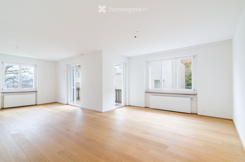 Empty room with light wooden flooring, white walls, multiple windows, and radiators. No furniture or equipment present.