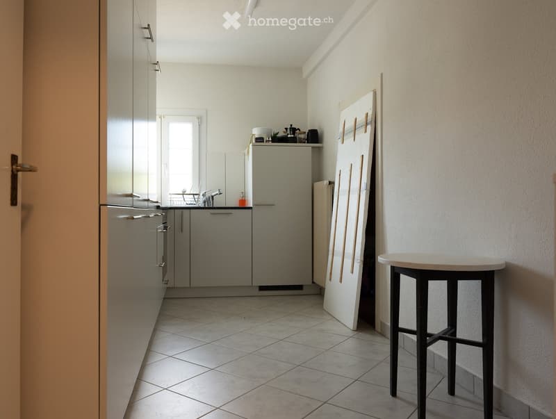A modern kitchen with tiled flooring, white cabinets, a stainless steel sink, and a small black stool near the wall.