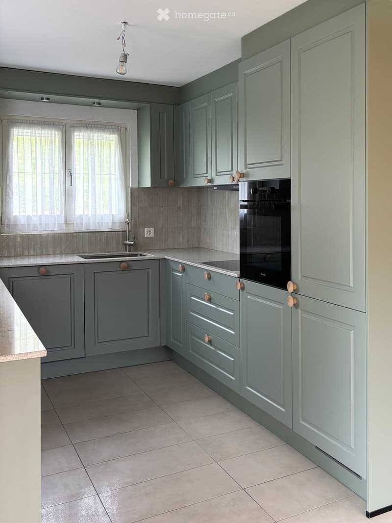 Modern kitchen with grey cabinets, a sink, and an oven, featuring tiled backsplash and tiled flooring.