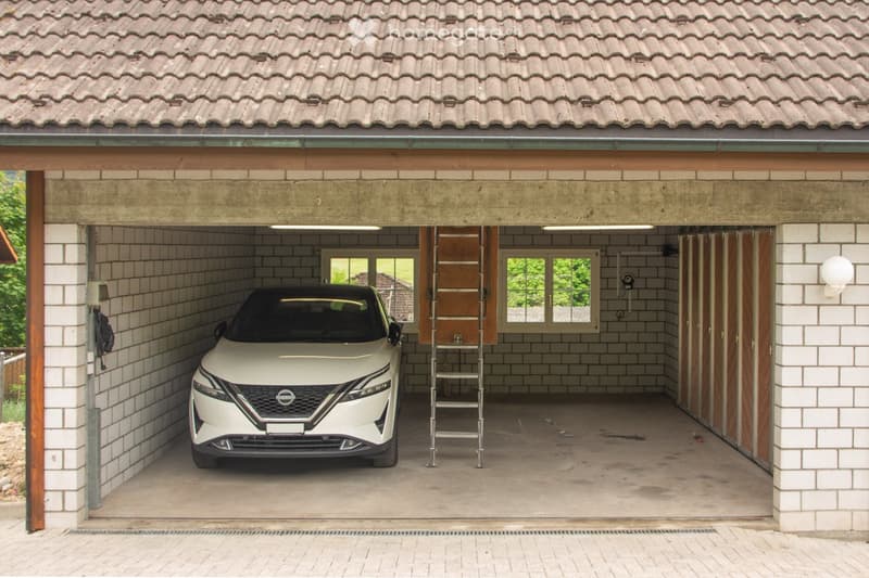 Attached garage with tiled roof, white tiled walls, and a white Nissan car parked inside. The garage has wooden trim, a ladder, and windows showing greenery outside.