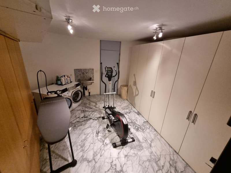Exercise bike, washing machine, sink, and cabinet in a room with marble flooring and white walls.