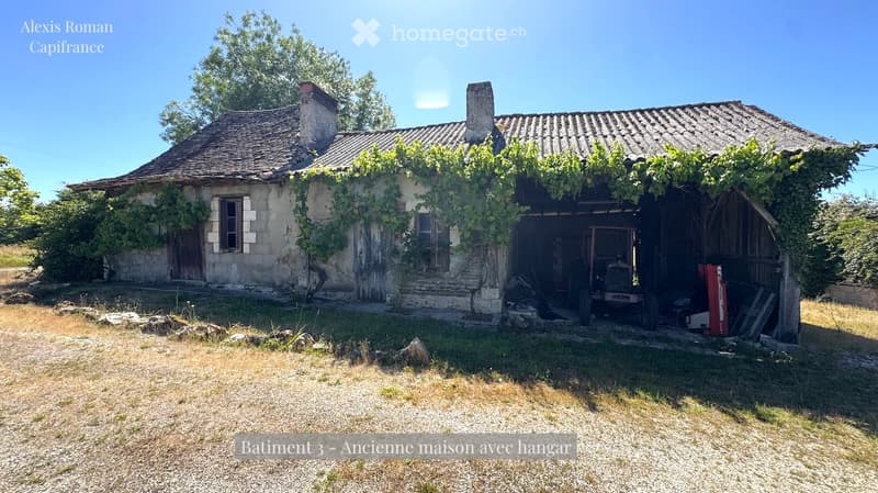 Old stone house with tiled roof, covered wooden garage, overgrown vegetation, and a tractor inside.