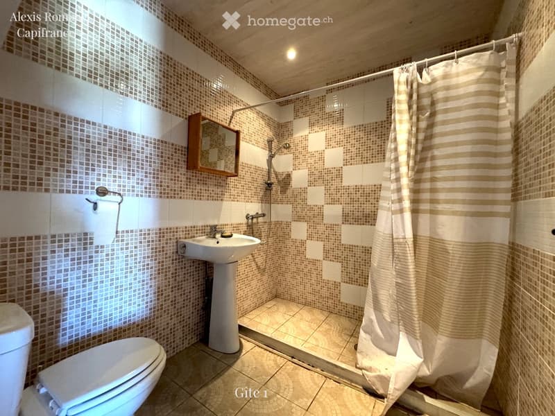 Modern bathroom with beige tiles, a toilet, a sink, a mirror, and a shower area with a curtain.