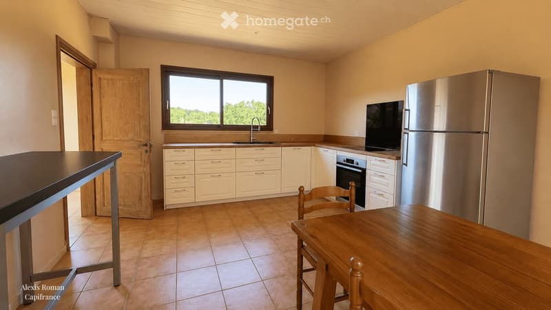 Bright kitchen with white cabinets, stainless steel appliances, a large window, and a wooden dining table with chairs.