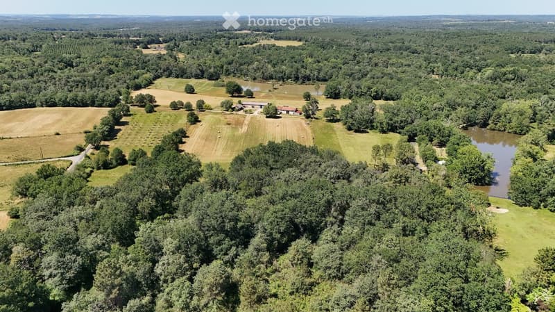Aerial view of a rural landscape with fields, trees, a small pond, and a few buildings in the distance.