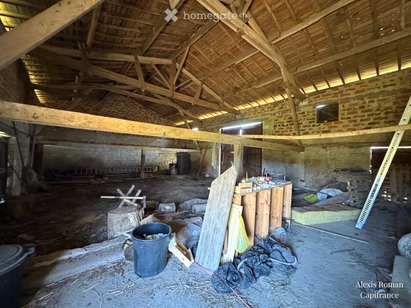 Empty room with exposed wooden beams and brick walls, construction materials scattered around, and a partially constructed wooden platform.