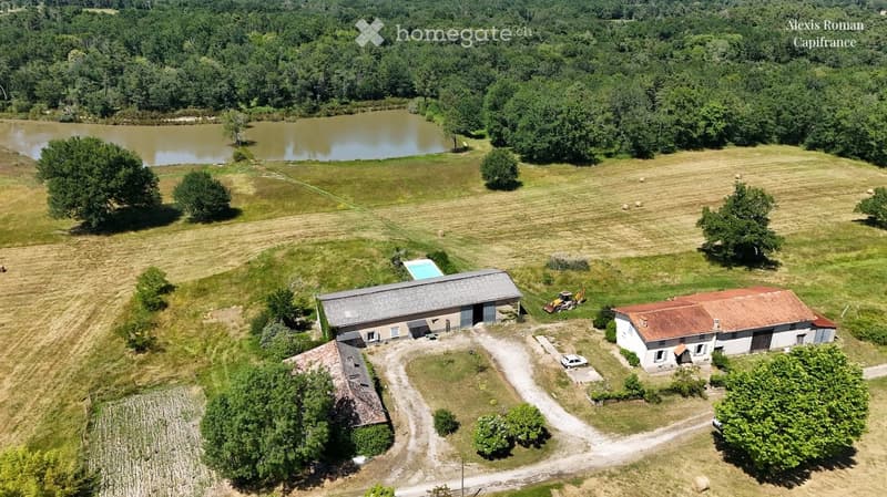 Aerial view of a rural property with a main house, outbuildings, a swimming pool, and surrounding fields and a pond.