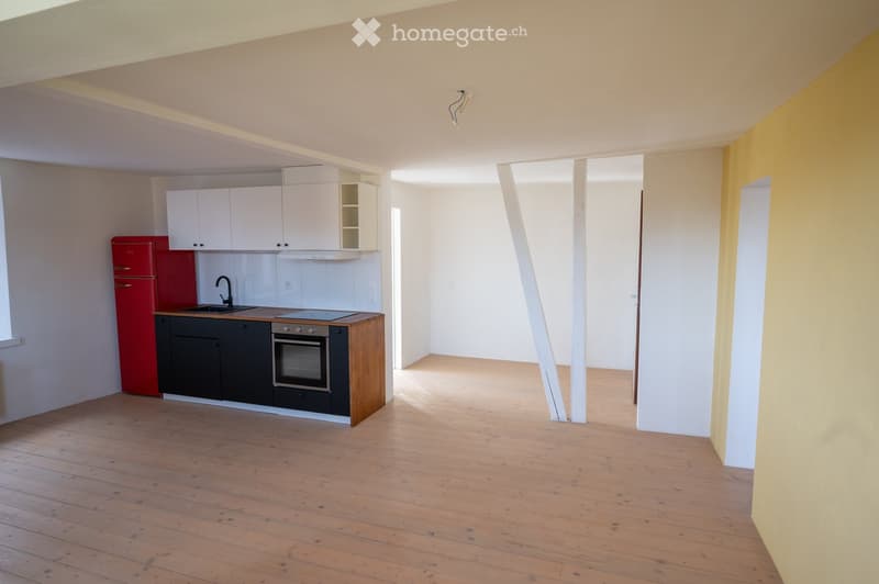 Modern kitchen with white cabinets, red refrigerator, wooden countertop, and black appliances. The space features wooden flooring and ample natural light.