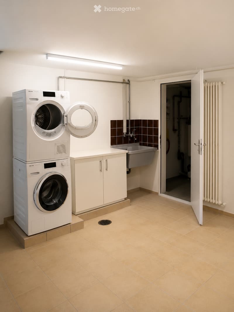 Clean, modern bathroom with tiled floor, white walls, a washing machine and dryer stacked, a sink, and a cabinet.