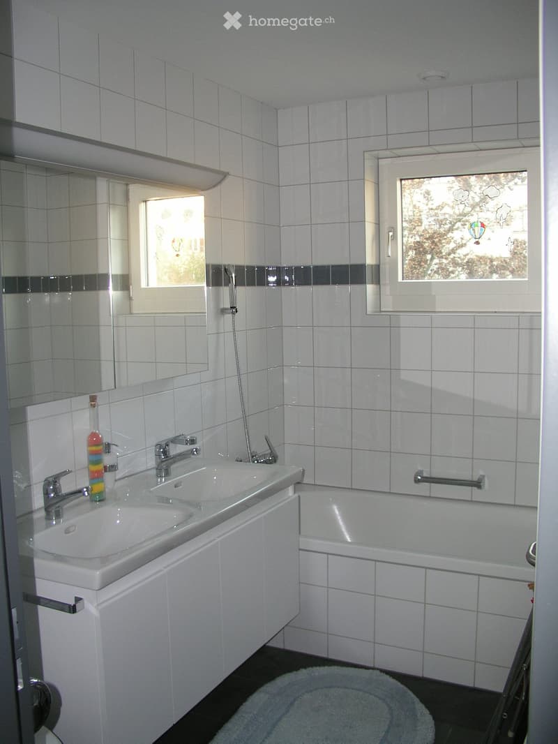 Modern bathroom with white tiles, double sink, bathtub, and large windows with decorative glass.