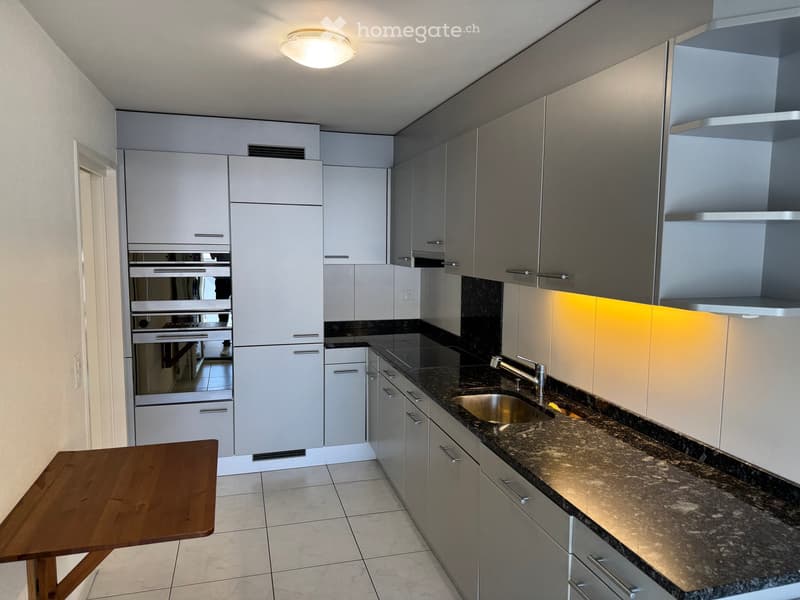 Modern kitchen with grey cabinets, granite countertop, stainless steel sink, and a wooden table.