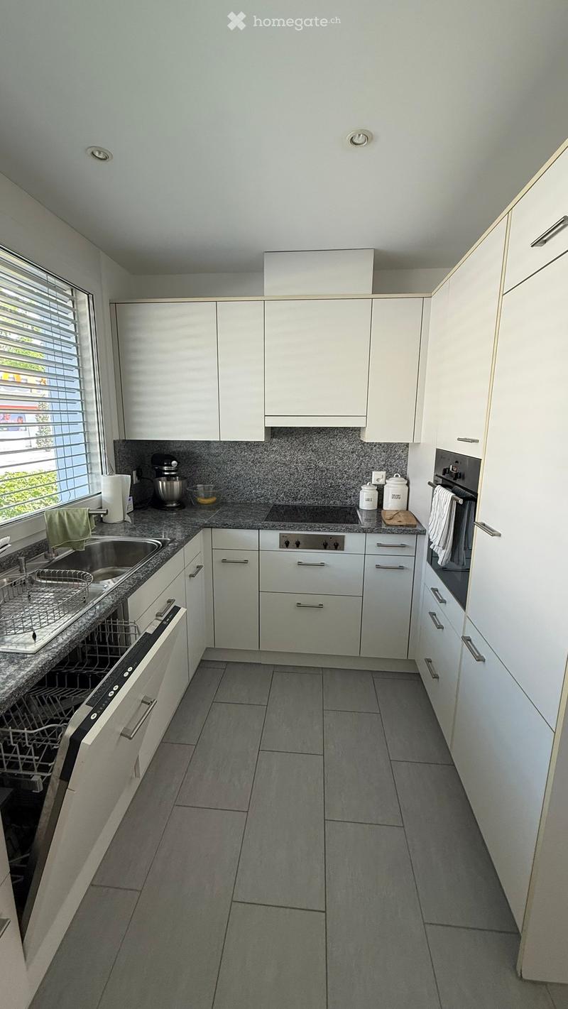 Modern kitchen with white cabinets, granite countertops, stainless steel appliances, and a large window with blinds.