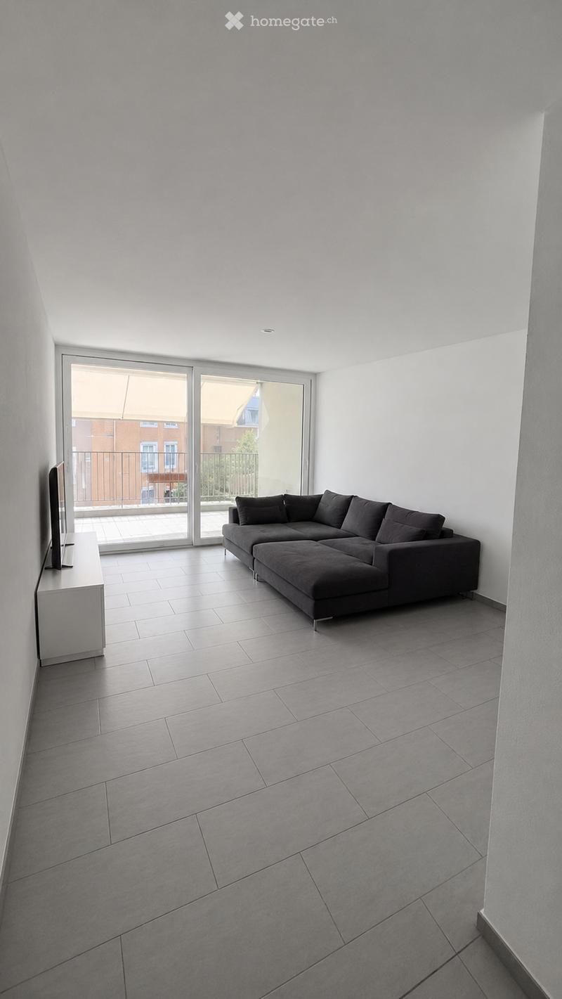 Modern living room with grey sectional sofa, flat-screen TV on a white stand, large sliding glass doors leading to a balcony.