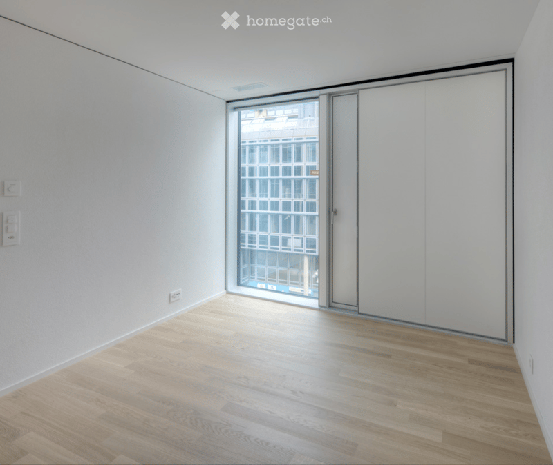Empty room with light wooden flooring, white walls, and large glass window with sliding doors.