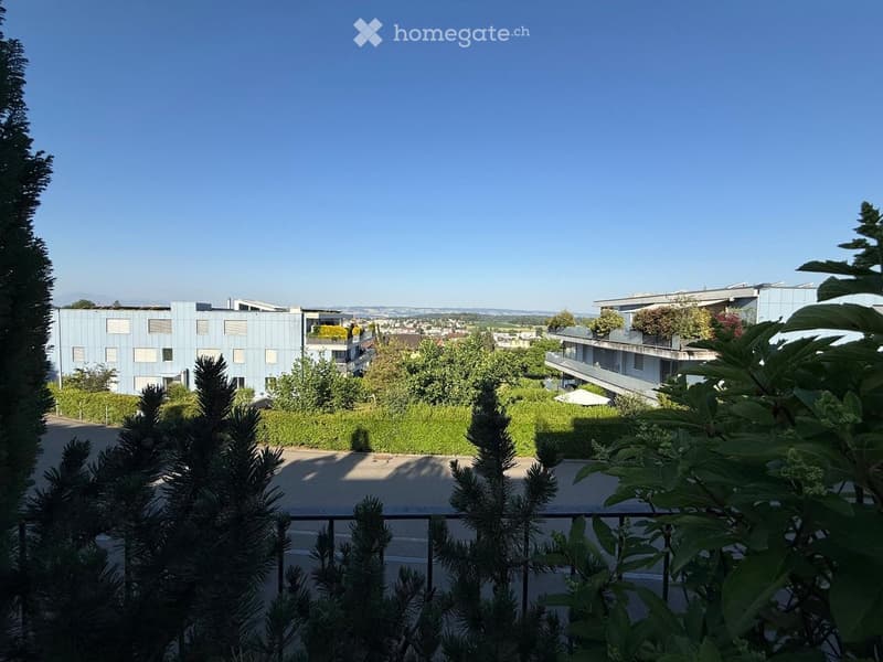 Balcony view overlooking a modern residential complex with multiple buildings, greenery, and a clear blue sky.