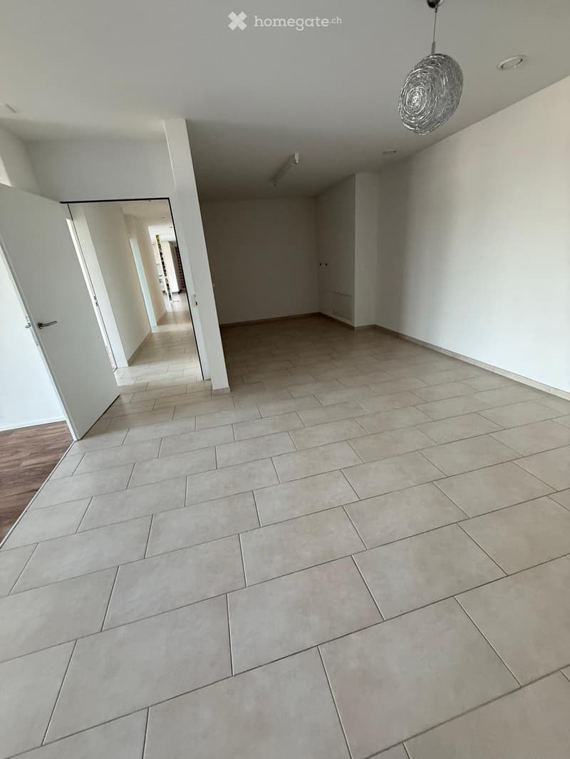 Empty room with tiled floor and white walls, featuring a hanging light fixture and an open doorway leading to another area.