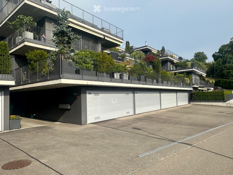 Modern multi-story building with balconies, garage, and surrounding greenery.