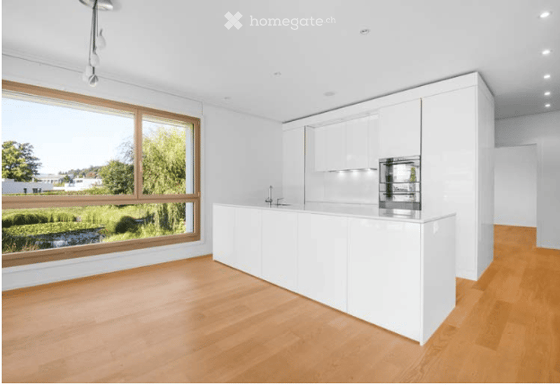 Modern kitchen with white cabinets, a central island, and large windows offering a scenic view of greenery outside.
