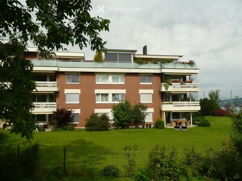 A two-story brick house with multiple balconies, large windows, and a well-maintained lawn in front.