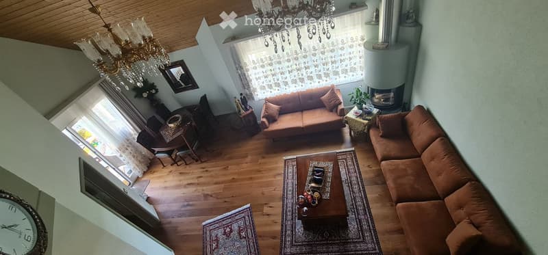 Living room with wooden flooring, two sofas, coffee table, dining area with chairs and table, chandelier, fireplace, and decorative items.