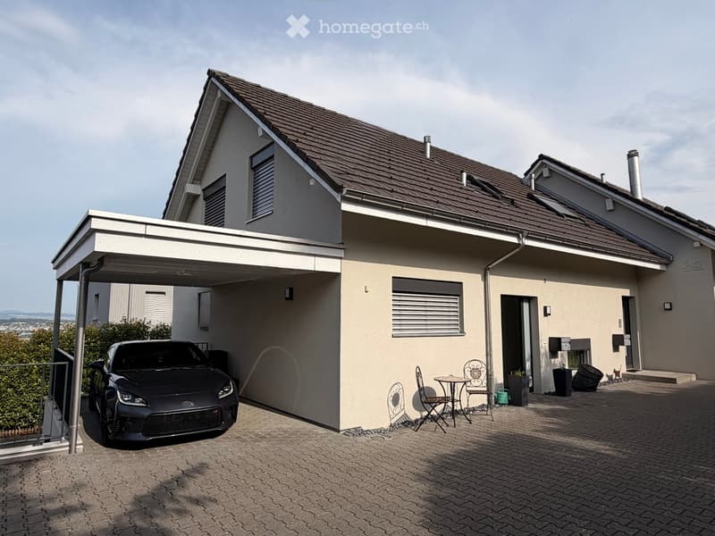 Two-story house with a garage, covered carport, and outdoor seating area with a small table and chairs.