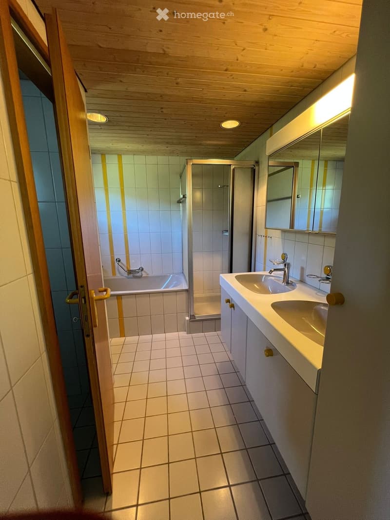 Modern bathroom with white tiled walls and floor, double sink vanity, large mirror, bathtub, and separate shower stall.