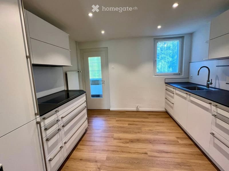 Modern kitchen with white cabinets, dark countertops, and wooden flooring. Features a sink with a modern faucet and built-in lighting.