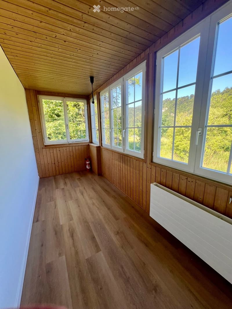 Empty room with wooden flooring, wooden paneling, large windows, and a radiator. No furniture or equipment present.