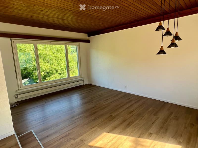Empty room with wooden flooring, white walls, large windows, and hanging pendant lights.
