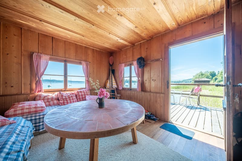 wooden walls, wooden table, couch with pillows, flower vase, door leading to balcony, ocean view