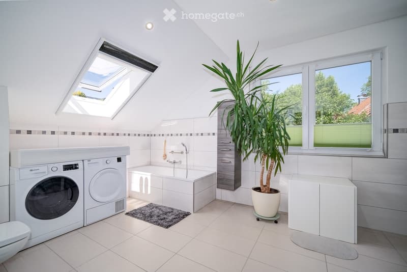modern bathroom with white tile flooring, white appliances, skylight, potted plant, bathtub, washer, dryer, toilet