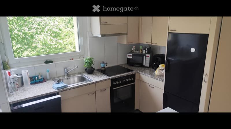 Modern kitchen with light wood cabinets, granite countertops, stainless steel sink, oven, microwave, refrigerator, and various kitchen items.
