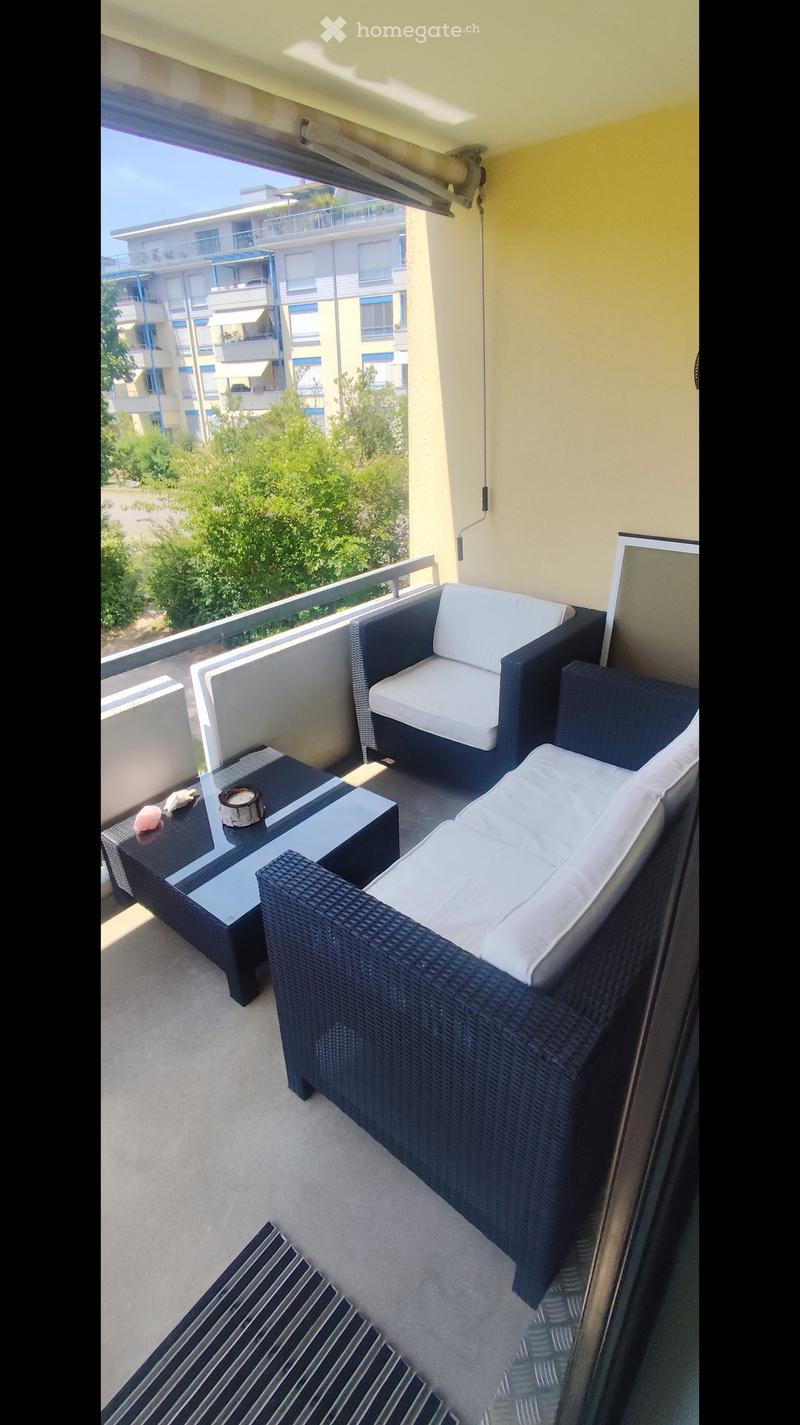 Balcony with a black wicker sofa, white cushions, a black glass coffee table, and a striped rug.