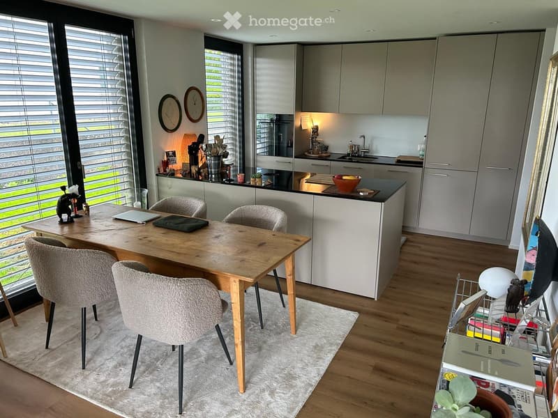 Modern kitchen with a wooden dining table, four chairs, grey cabinets, a sink, and various kitchen items on the counter.