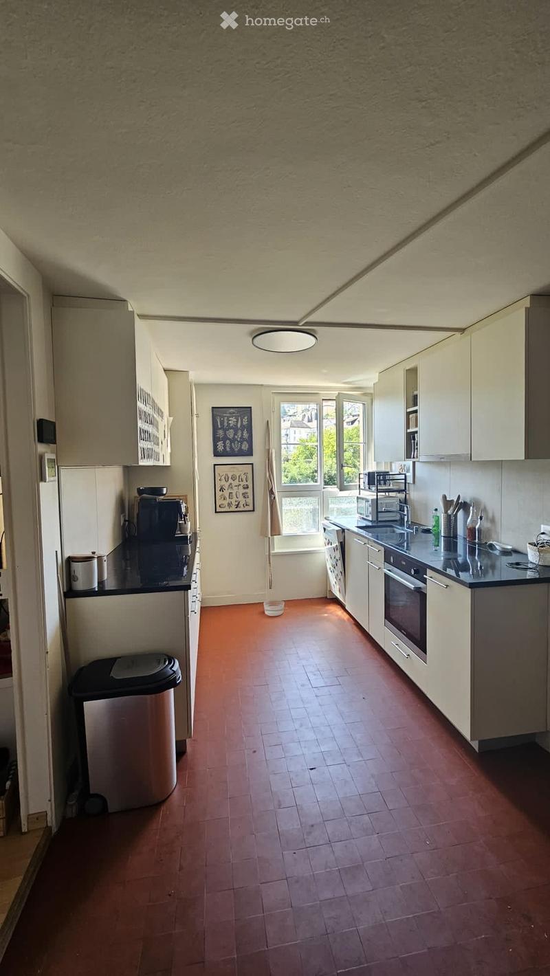 Modern kitchen with white cabinets, stainless steel appliances, and a red tiled floor. Features include a refrigerator, oven, microwave, sink, and various kitchen items on the countertops.