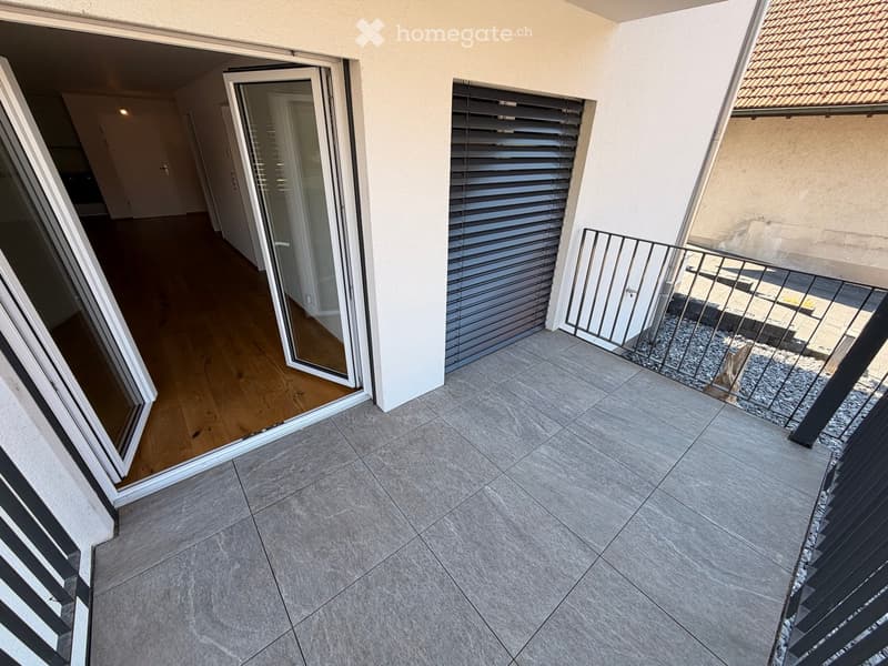 Balcony with tiled floor, metal railing, sliding glass doors leading to interior, and blinds on windows.