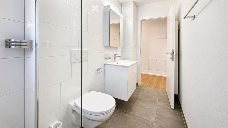 Modern bathroom with white tiles, a toilet, a sink with a mirror, and a glass shower enclosure.