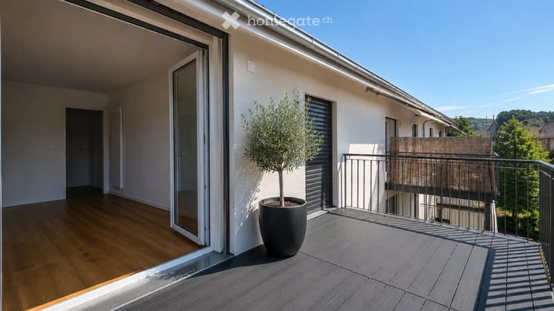 Balcony with wooden decking, metal railing, potted tree, and sliding glass door leading to interior space.