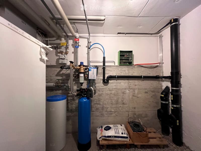 Utility room with water tank, water filter, pipes, valves, and a toolbox on a wooden pallet.