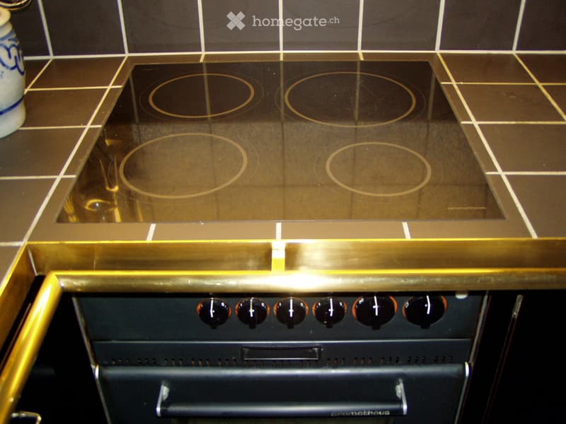 Induction cooktop with four circular cooking zones and control knobs below, placed on a tiled countertop.